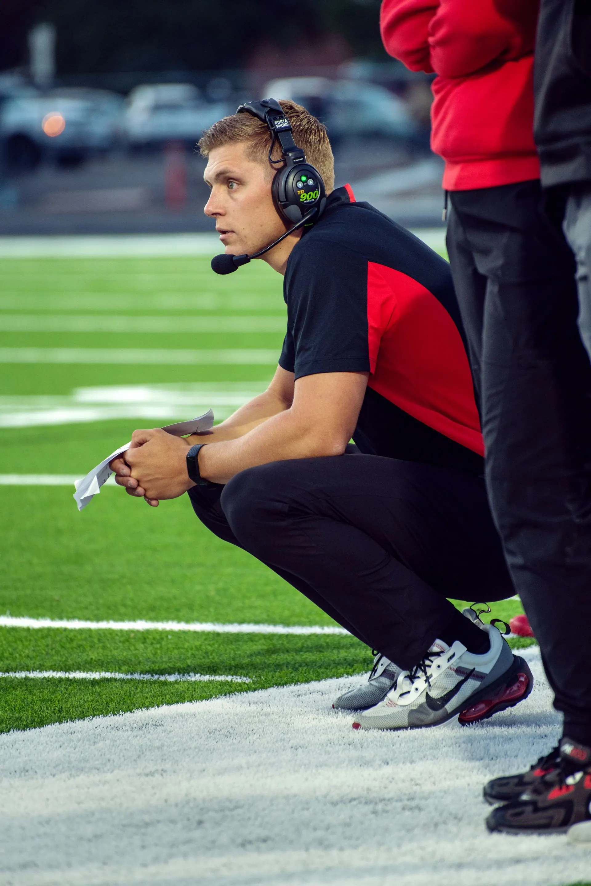 Trainer mit Headset kniet an der Seitenlinie